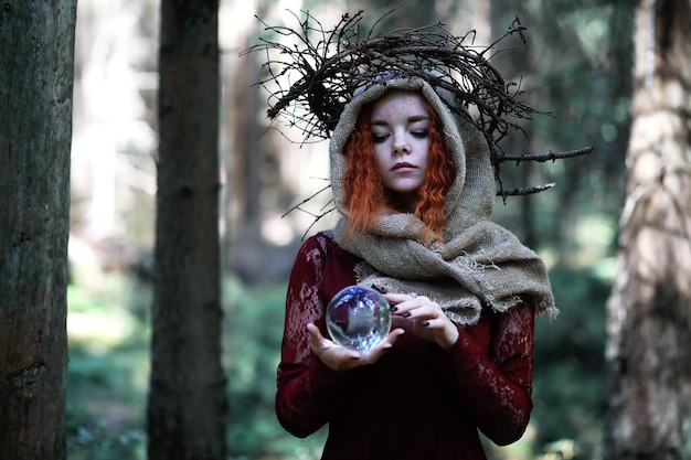 La bruja pelirroja realiza un ritual con una bola de cristal en el bosque.