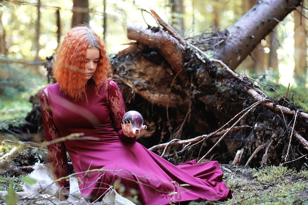 La bruja pelirroja realiza un ritual con una bola de cristal en el bosque.