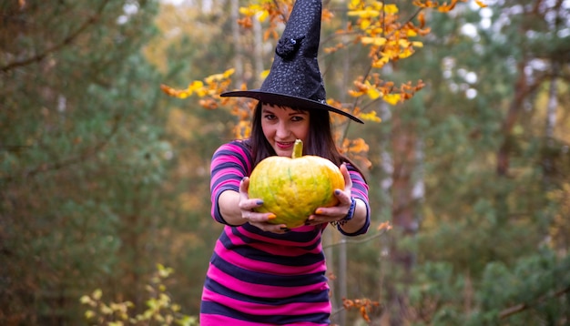 Bruja sostiene una calabaza a la cámara en el bosque de otoño