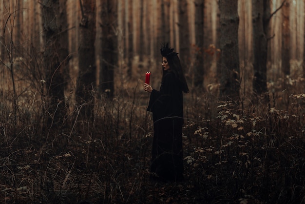 Bruja terrible oscura con velas en sus manos realiza un ritual místico oculto en el bosque