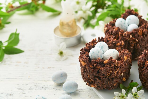 Brunch o desayuno de Pascua Pastel de nido de chocolate de Pascua con huevos de chocolate dulces tradicionales bollos cruzados calientes y huevos rellenos con ramos de manzanos en flor Concepto de comida de vacaciones de Pascua de primavera