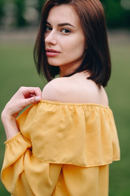 Brunette auf einem natürlichen Hintergrund Ohne Make-up in einer gelben Bluse Vertikales Porträt