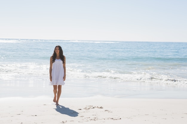 Brunette em vestido de sol branco andando do mar