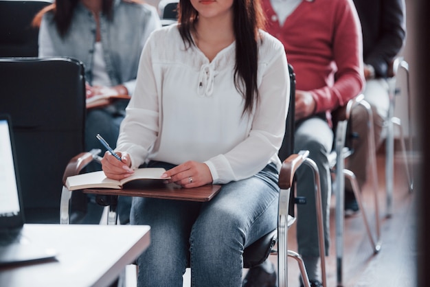 Brunette escucha atentamente. Grupo de personas en conferencia de negocios en el aula moderna durante el día