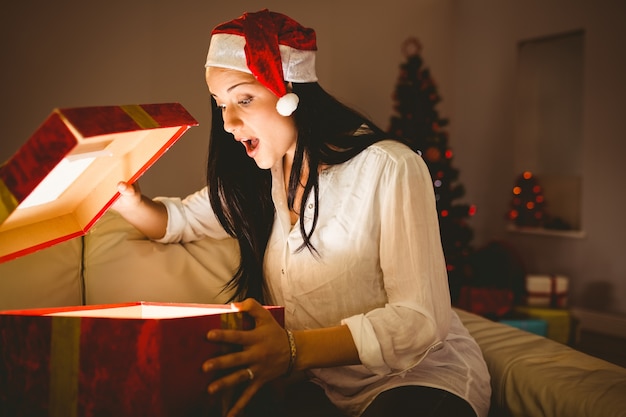 Brunette festivo que abre um presente brilhante de Natal