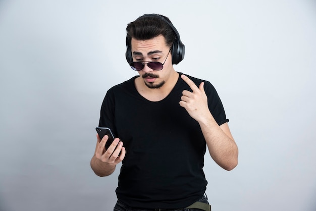 Brunette Mann Modell in Sonnenbrille und Kopfhörer halten Handy.