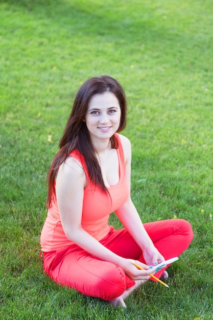 Brunettee Mädchen mit Notizbuch auf grünem Gras im Park.