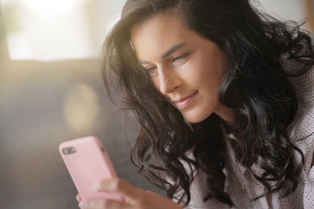 Brunettefrau, die auf dem Sofa, angeschlossen mit Smartphone sich entspannt