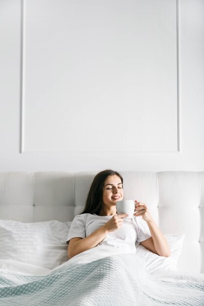 Brunettefrau, die Kaffee am Bett trinkt