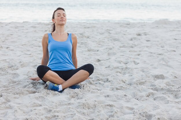 Brunettefrau, die nach Sport am Strand sitzt