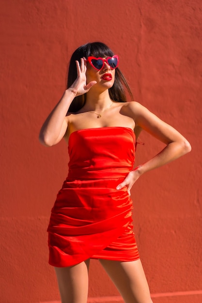 Brunettemädchen auf einem roten Hintergrund mit Herzgläsern und rotem festem Kleid Valentinstag