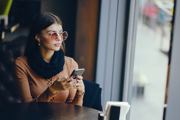 Brunettemädchen, das ihr Handy beim Sitzen an einem rastaurant für das Mittagessen verwendet