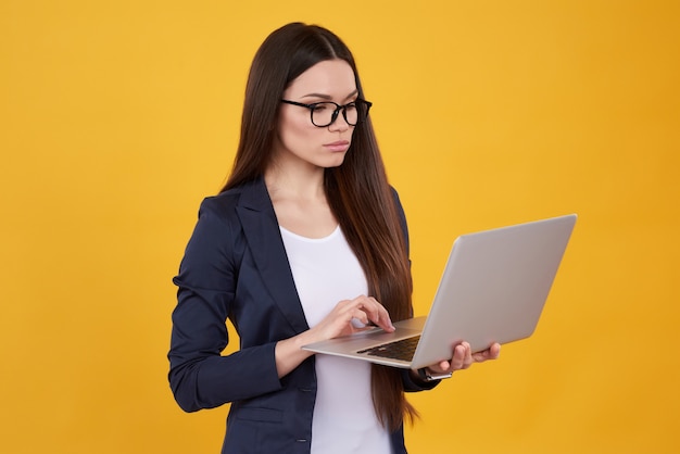 Brunettemädchen in der Klage wirft mit Laptop in den Gläsern auf.