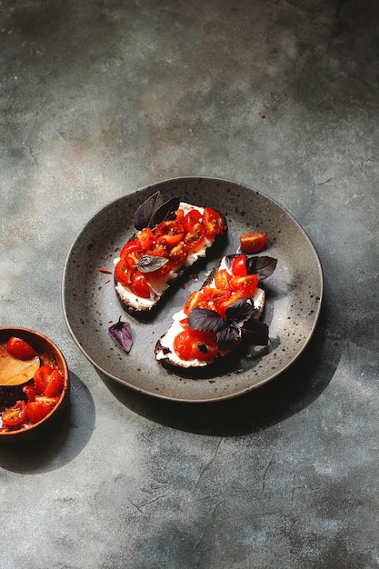 Bruschett con tomates cherry requesón albahaca hierbas ajo sellado sobre fondo gris luz dura natural