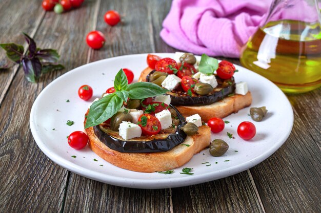 Bruschetta de ajo con berenjena, queso feta, tomates cherry, alcaparras. Útil aperitivo vegetariano. Cocina italiana.