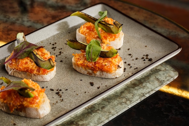 Bruschetta al horno con queso de salmón, tomates secos y aguacate en plato gris sobre fondo brillante