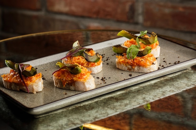 Foto bruschetta al horno con queso de salmón, tomates secos y aguacate en plato gris sobre fondo brillante