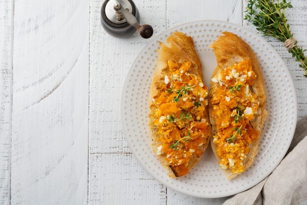 Bruschetta con calabaza al horno, queso feta y tomillo sobre fondo de madera clara Sándwich de calabaza picante