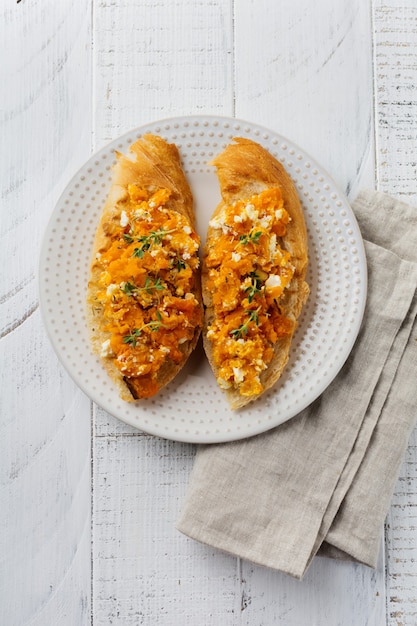 Foto bruschetta con calabaza al horno, queso feta y tomillo sobre superficie de madera clara. sándwich de calabaza picante. enfoque selectivo. vista superior.