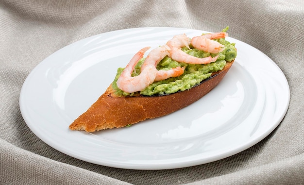 Bruschetta con camarones y mousse de aguacate en un plato blanco sobre un fondo textil