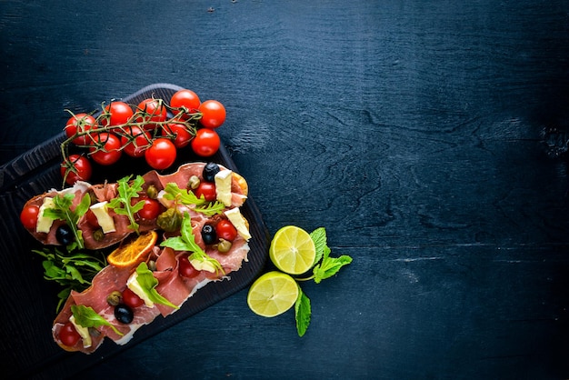 Bruschetta con carne, aceitunas, hierbas y queso parmesano sobre pan, bocadillos fríos, cocina italiana sobre fondo de madera