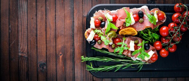 Bruschetta com carne, azeitonas, ervas e queijo parmesão no pão. Petiscos frios. Cozinha italiana. No fundo de madeira.