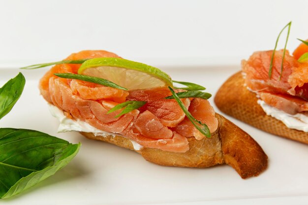 Bruschetta com limão de peixe vermelho e ervas em um prato branco Lanche saudável e saboroso Closeup