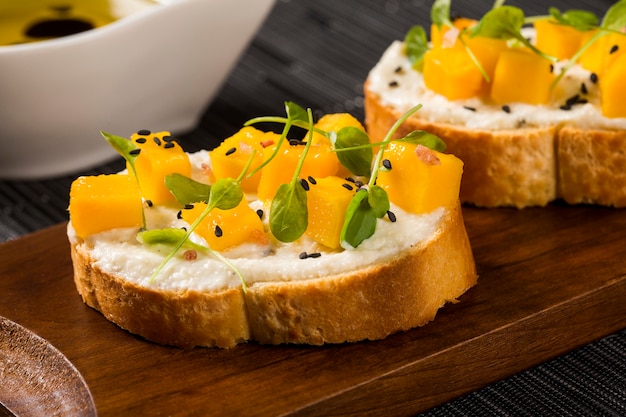 Bruschetta com manga picada, agrião, manjericão e queijo de cabra na baguete fresca sobre a mesa