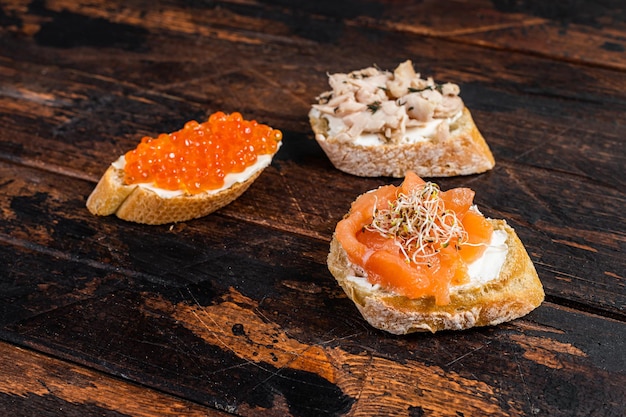 Bruschetta com salmão defumado a quente, caviar vermelho e ervas. Fundo de madeira. Vista do topo.