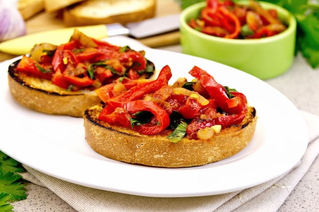 Bruschetta com tomate assado, pimentão, alho, cebola e salsa em um prato branco sobre um guardanapo sobre uma mesa de granito de fundo