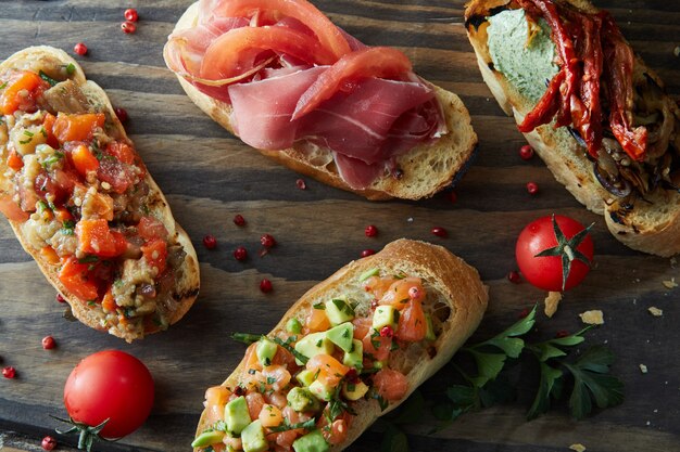 Bruschetta italiana con tomates asados, aguacate, salmón, jamón, pimientos, hierbas sobre una tabla de madera