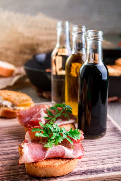 Bruschetta con jamón y rúcula cerca de la botella con salsa sobre fondo de madera