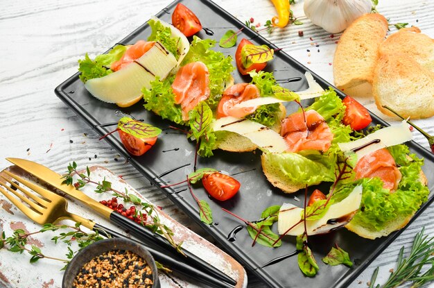 Bruschetta con lechuga de salmón y queso parmesano en un plato negro Vista superior Estilo rústico