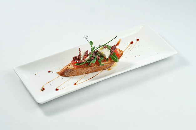 Bruschetta mit getrockneten Tomaten und Feta in einem weißen Teller auf einer weißen Tischdecke