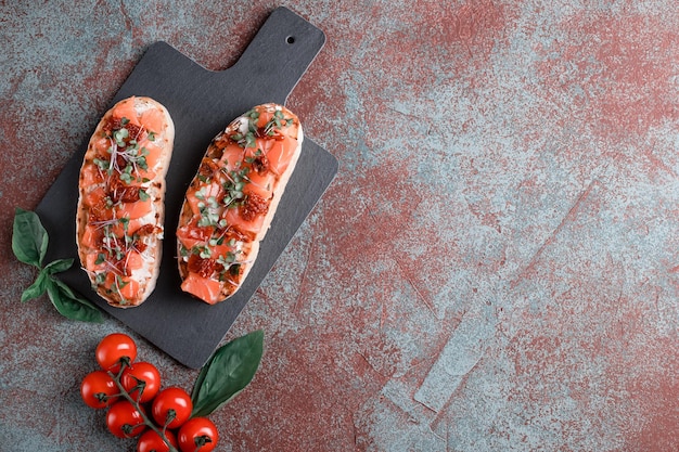 Bruschetta mit Lachs, getrockneten Tomaten, Kräutern, Hüttenkäse, auf Betongrund, Holzbrett