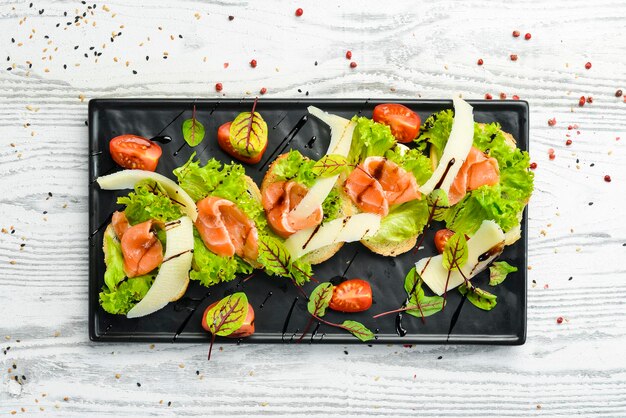 Bruschetta mit Lachs, Salat und Parmesankäse auf einem schwarzen Teller. Ansicht von oben. Rustikaler Stil.