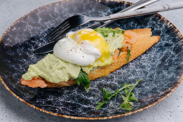 Bruschetta mit Lachssalat und pochiertem Ei auf einem Teller mit Besteck