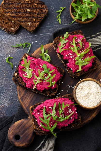 Bruschetta mit Rote-Bete-Hummus, Rucola und Sesam auf dunkler Betonoberfläche