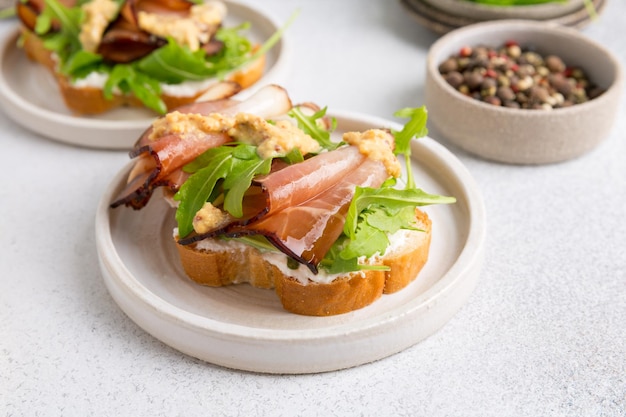 Bruschetta mit Schinken und Rucola auf einem Teller. Heller Hintergrund.