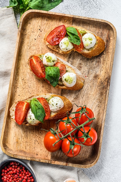 Bruschetta mit Tomaten, Mozzarella und Basilikum. italienische Vorspeise oder Snack, Antipasti. grauer Hintergrund. Draufsicht