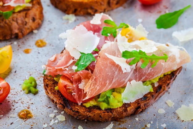 Bruschetta con prosciutto aguacate tomates rúcula y queso parmesano