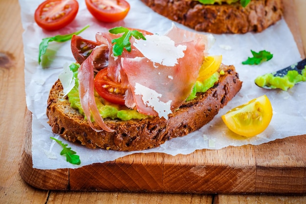 Bruschetta con prosciutto aguacate tomates rúcula y queso parmesano