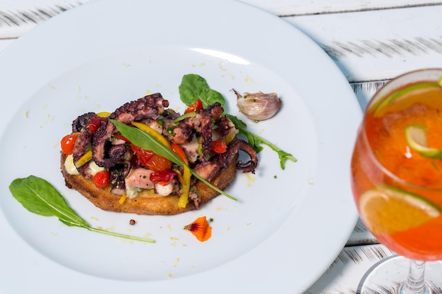 Bruschetta de pulpo con ajo asado y rúcula con bebida tropical. Vista desde arriba