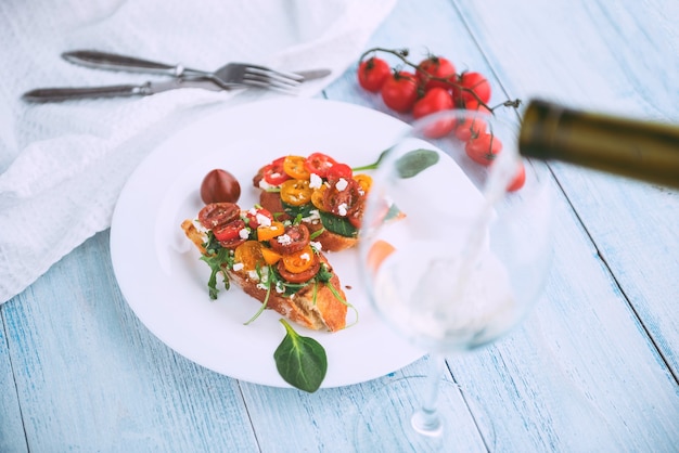 Bruschetta con queso, albahaca, rúcula y tomates cherry y una copa de vino blanco