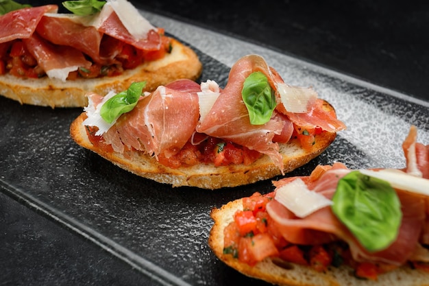 Bruschetta salada con jamón de salmón y queso parmesano sobre fondo oscuro