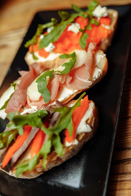 Bruschetta con salmón, requesón, tomates secos y microvegetales, sobre un fondo negro.