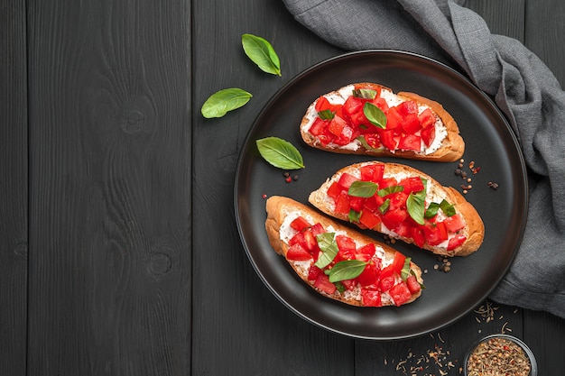 Bruschetta con tomate, mantequilla, albahaca y queso sobre fondo negro. Vista superior, espacio de copia.