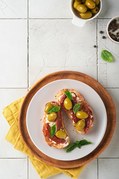 Bruschetta con tomates secados al sol Tostadas o sándwich con ricotta tomates secados al sol y hierbas de Provenza con albahaca servida en un plato sobre una mesa de baldosas viejas grises Receta del menú del banner de la vista superior