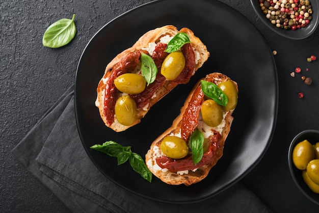 Bruschetta con tomates secados al sol Tostadas o sándwich con ricotta tomates secados al sol y hierbas provenzales con albahaca servida en un plato negro sobre una mesa de fondo negro Receta del menú del banner de la vista superior