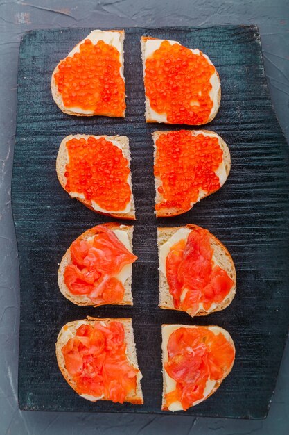 Bruschetta con trucha y caviar rojo en una pizarra negra.